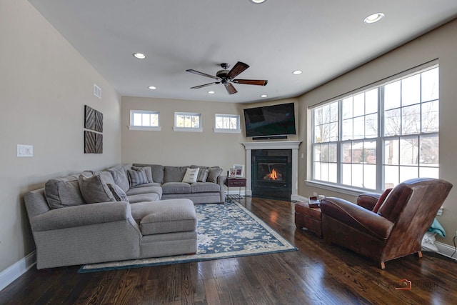 living room featuring visible vents, baseboards, dark wood finished floors, and a glass covered fireplace