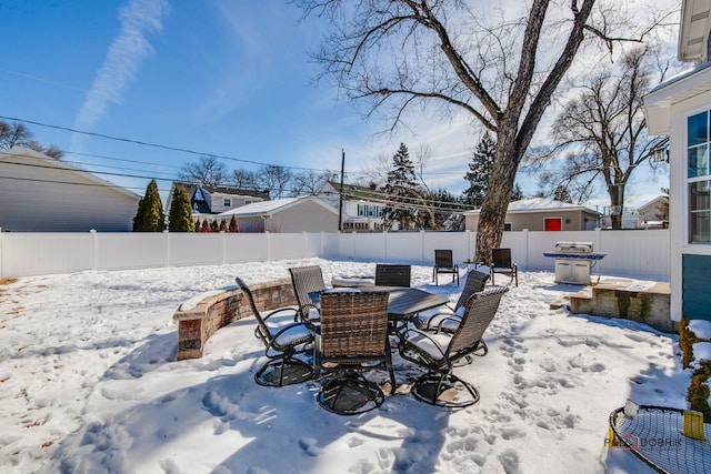 snow covered patio with a fenced backyard and area for grilling