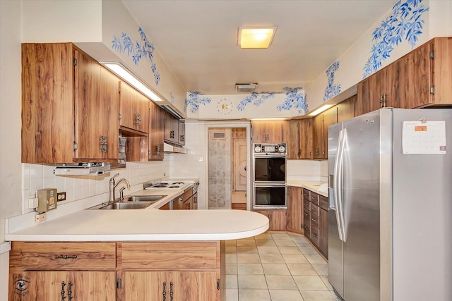 kitchen featuring light tile patterned floors, light countertops, a sink, stainless steel fridge, and a peninsula