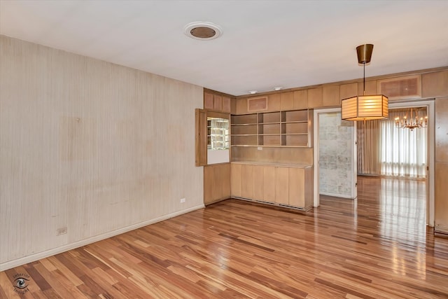 spare room featuring baseboards, light wood finished floors, and a notable chandelier