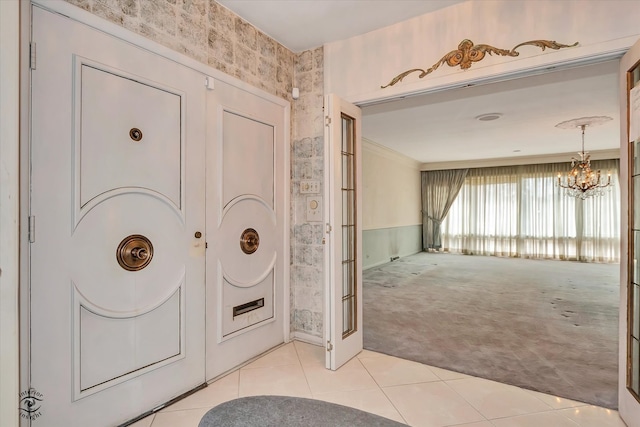 foyer entrance featuring light tile patterned floors, wallpapered walls, light colored carpet, ornamental molding, and a notable chandelier