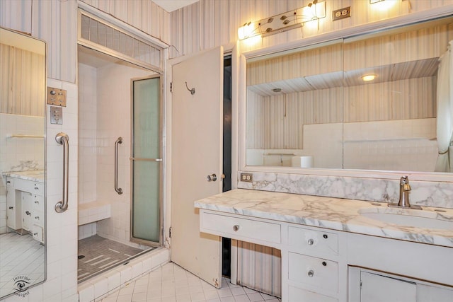 bathroom with wallpapered walls, a shower stall, tile patterned flooring, and vanity