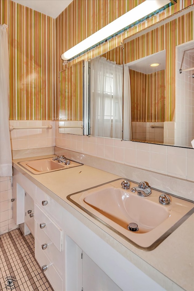 full bathroom featuring double vanity, wallpapered walls, and a sink