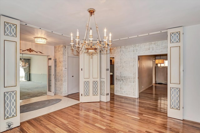 unfurnished room with wallpapered walls, wood finished floors, and an inviting chandelier