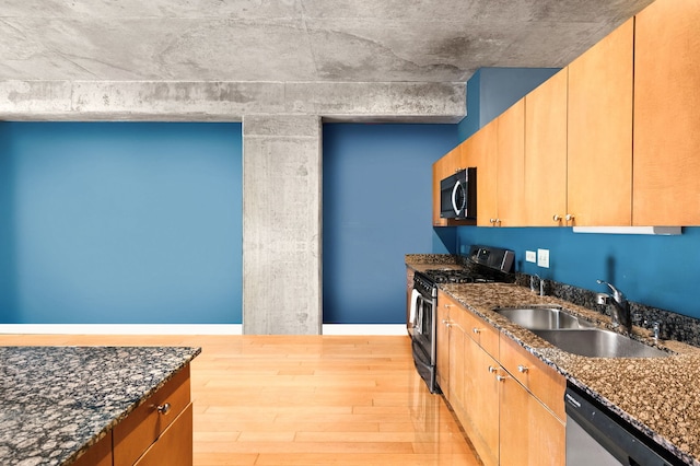 kitchen featuring brown cabinets, dark stone countertops, stainless steel appliances, light wood-type flooring, and a sink