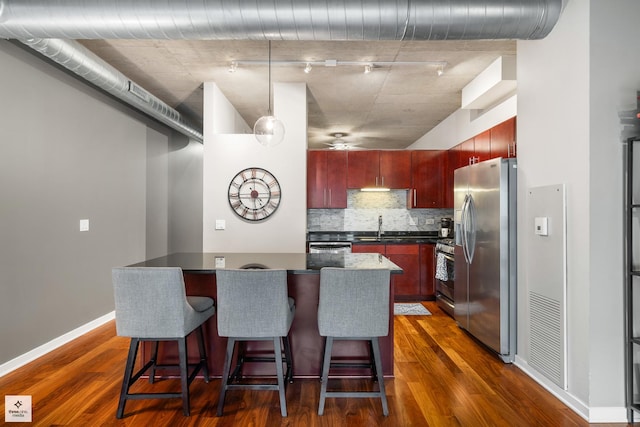 kitchen with appliances with stainless steel finishes, sink, a kitchen breakfast bar, dark wood-type flooring, and tasteful backsplash