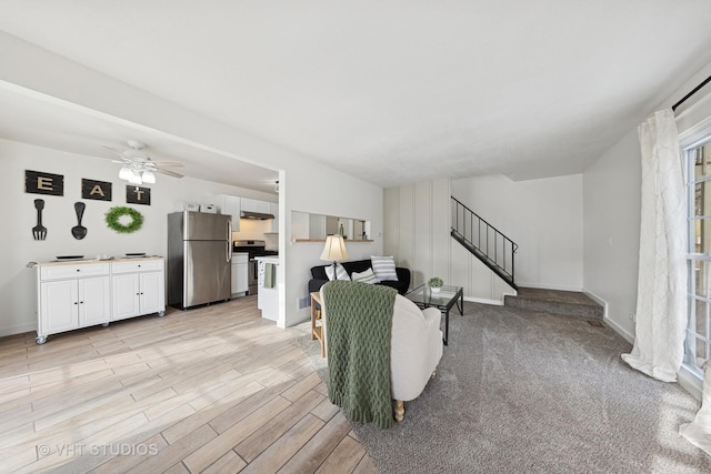 living area with baseboards, stairway, a ceiling fan, and light wood-style floors