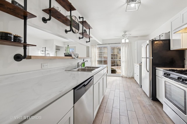 kitchen with white cabinets, light stone counters, stainless steel appliances, open shelves, and a sink