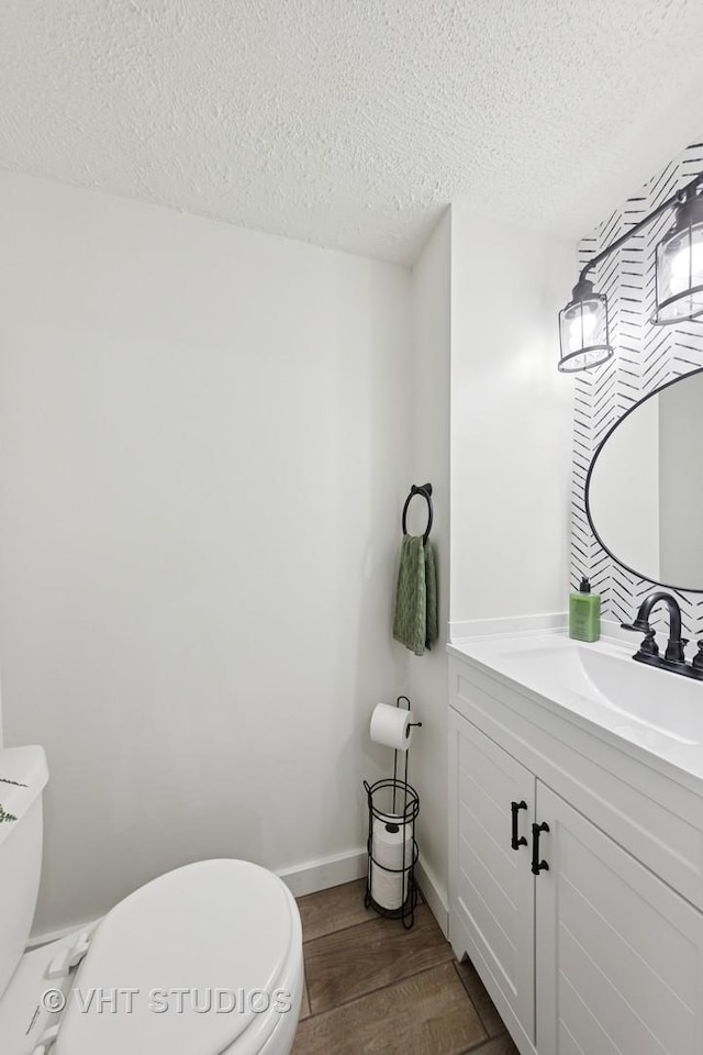 bathroom featuring toilet, a textured ceiling, vanity, wood finished floors, and baseboards