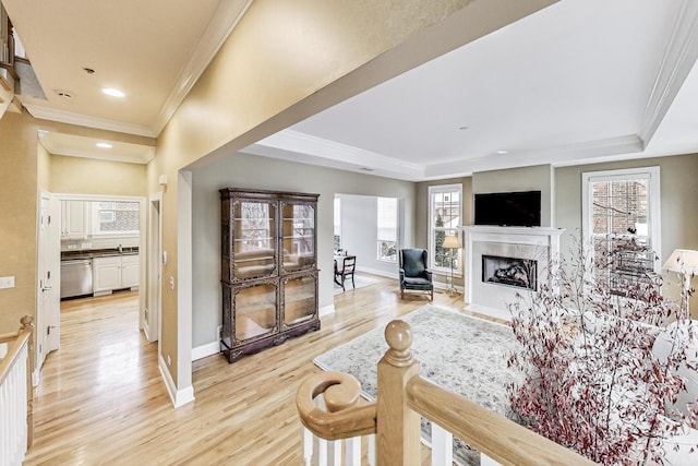 living area with light wood finished floors, a fireplace with flush hearth, a tray ceiling, and baseboards