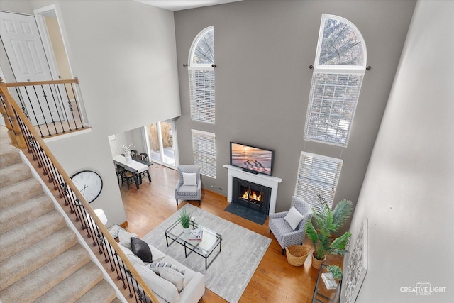 living area with a fireplace with flush hearth, a high ceiling, stairway, and wood finished floors