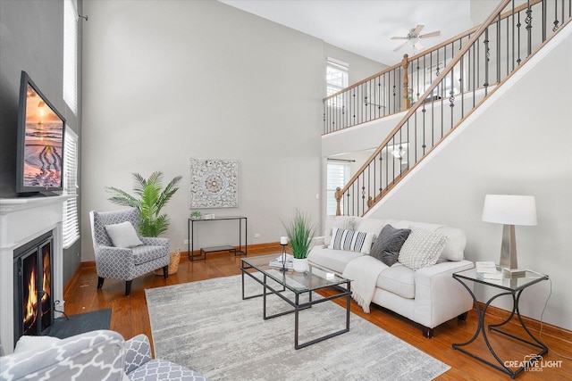 living area featuring a fireplace with flush hearth, a wealth of natural light, stairway, and wood finished floors