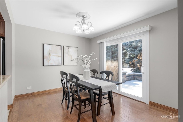 dining area featuring baseboards, light wood-type flooring, and an inviting chandelier