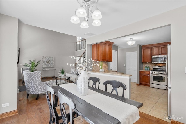 dining space with stairs, light tile patterned floors, visible vents, and an inviting chandelier