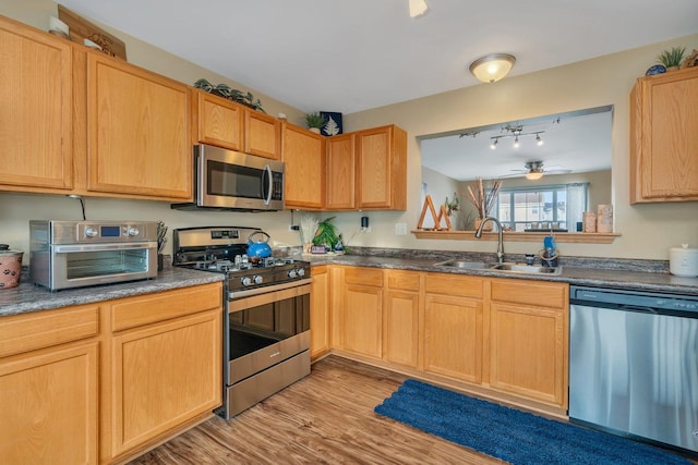 kitchen featuring appliances with stainless steel finishes, sink, light wood-type flooring, ceiling fan, and light brown cabinetry