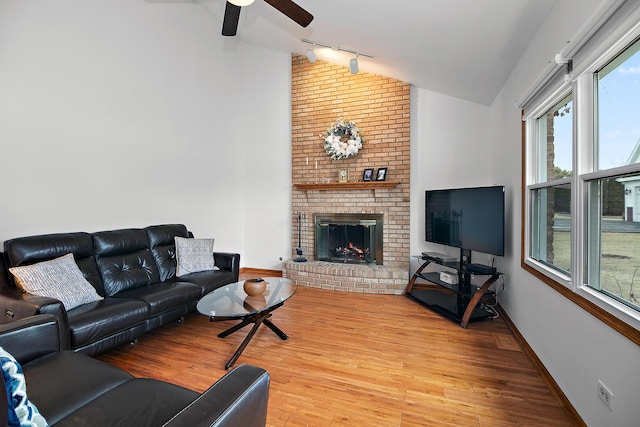 living room featuring a brick fireplace, vaulted ceiling, baseboards, and wood finished floors