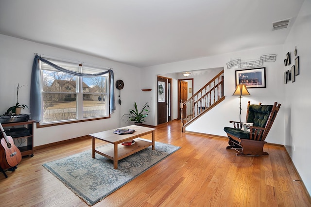 living area featuring light wood finished floors, baseboards, stairs, and visible vents