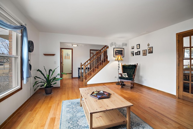 living area with light wood-type flooring, plenty of natural light, baseboards, and stairs