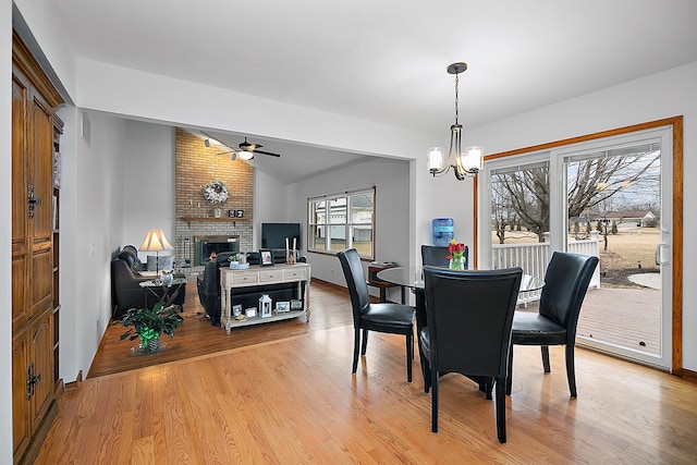 dining space featuring a fireplace, visible vents, vaulted ceiling, light wood-type flooring, and ceiling fan with notable chandelier