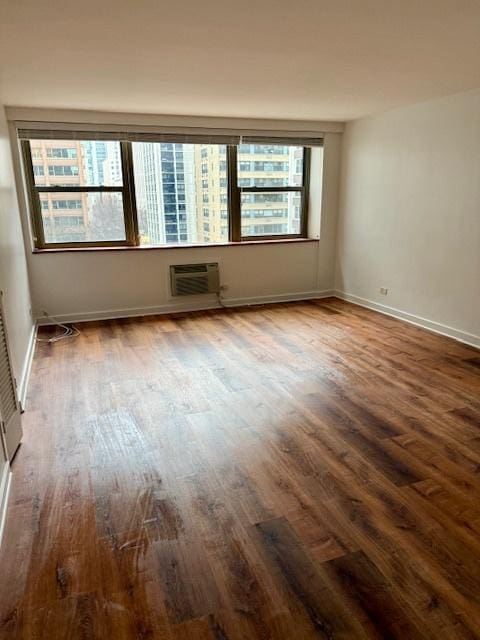 unfurnished room with dark wood-style flooring, a wall unit AC, and baseboards