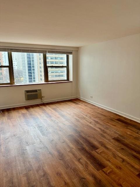 spare room with baseboards, dark wood finished floors, and an AC wall unit