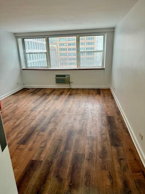 unfurnished room featuring baseboards, dark wood finished floors, and a wall mounted air conditioner