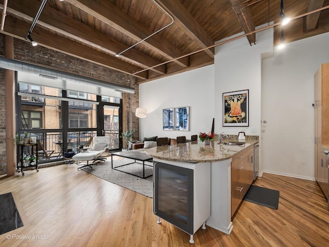 kitchen with light wood-type flooring, sink, light stone counters, and beam ceiling