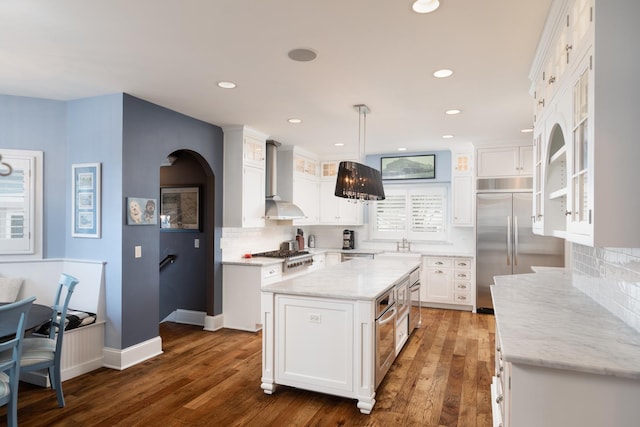 kitchen featuring white cabinetry, stainless steel appliances, hanging light fixtures, a center island, and wall chimney exhaust hood