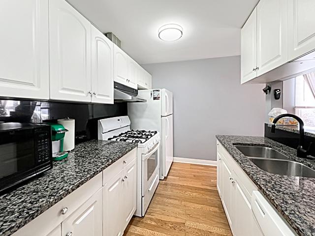 kitchen with under cabinet range hood, white appliances, a sink, white cabinets, and dark stone counters