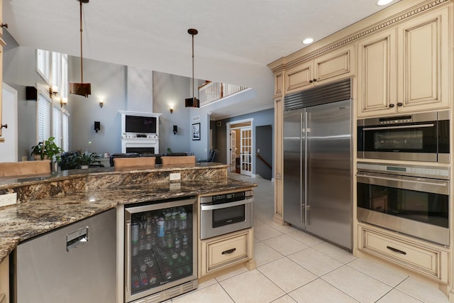 kitchen with wine cooler, light tile patterned floors, cream cabinets, appliances with stainless steel finishes, and dark stone countertops