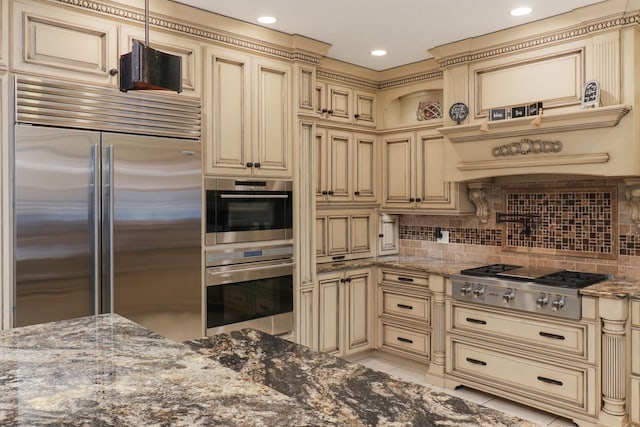 kitchen with tasteful backsplash, appliances with stainless steel finishes, dark stone counters, and cream cabinetry