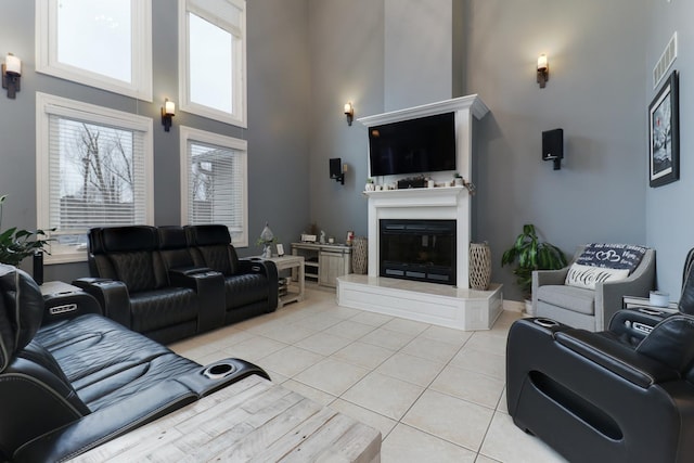 living area with a glass covered fireplace, visible vents, a high ceiling, and light tile patterned floors