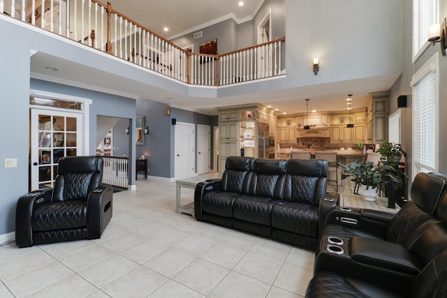 living area with light tile patterned floors, a high ceiling, visible vents, baseboards, and crown molding