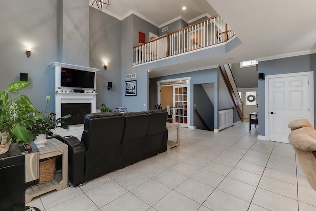 living room with light tile patterned floors, a fireplace, a high ceiling, and crown molding