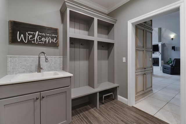 mudroom featuring light wood-style floors, a fireplace, ornamental molding, and a sink