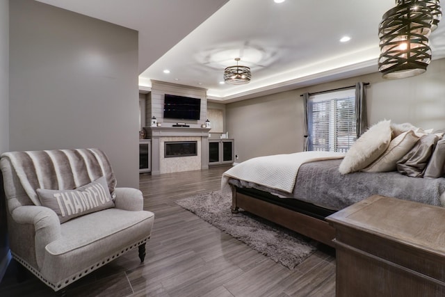 bedroom with a tray ceiling, a fireplace, wood finished floors, and recessed lighting