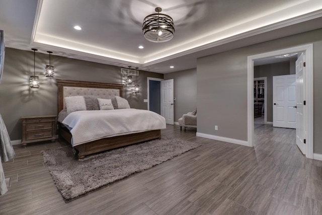 bedroom featuring a tray ceiling, wood finished floors, baseboards, and recessed lighting