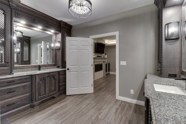 bathroom with baseboards, a tile fireplace, wood finished floors, a sink, and two vanities