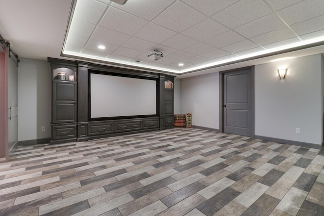 cinema room with a tray ceiling, a paneled ceiling, baseboards, and a barn door