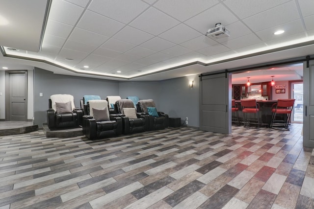 cinema with a paneled ceiling, a barn door, a tray ceiling, and recessed lighting