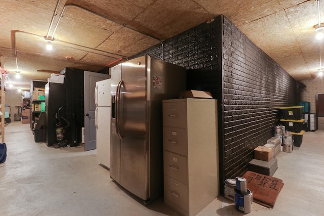 basement featuring brick wall and stainless steel fridge with ice dispenser