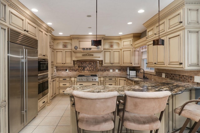 kitchen with cream cabinetry, light tile patterned floors, a sink, a peninsula, and built in refrigerator