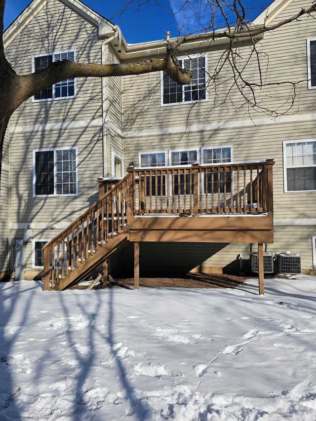 snow covered back of property with central AC unit and a wooden deck