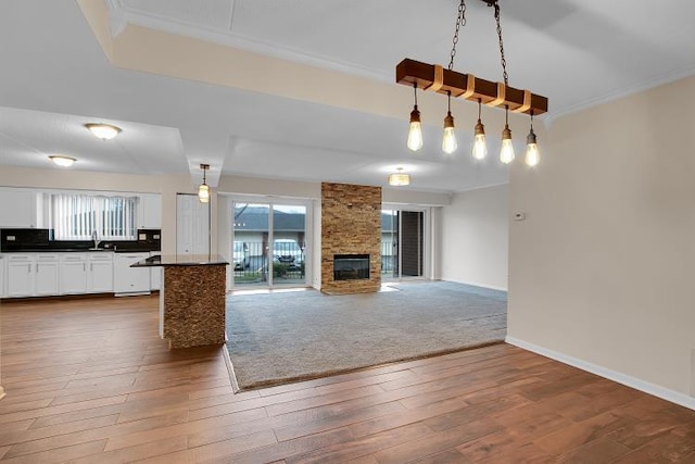 unfurnished living room featuring crown molding, a stone fireplace, dark hardwood / wood-style floors, and sink