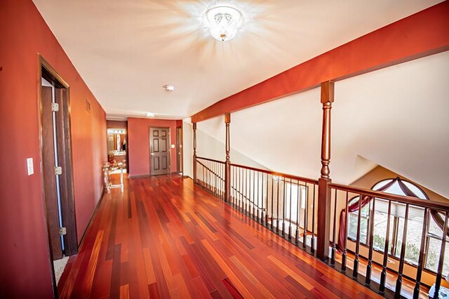 corridor with an upstairs landing, wood finished floors, and vaulted ceiling