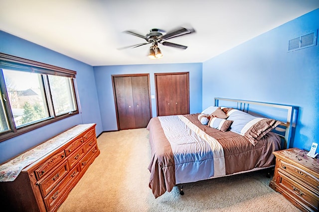 bedroom featuring visible vents, two closets, light colored carpet, and a ceiling fan