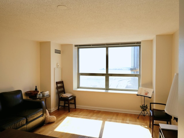 sitting room featuring light wood-type flooring, a healthy amount of sunlight, visible vents, and baseboards