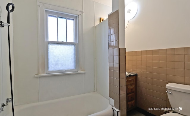 full bathroom featuring toilet, a wainscoted wall, tile walls, and a bath