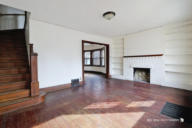 unfurnished living room featuring built in shelves, wood-type flooring, visible vents, a brick fireplace, and baseboards