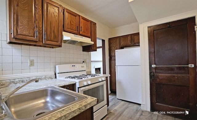 kitchen with under cabinet range hood, white appliances, a sink, light countertops, and decorative backsplash